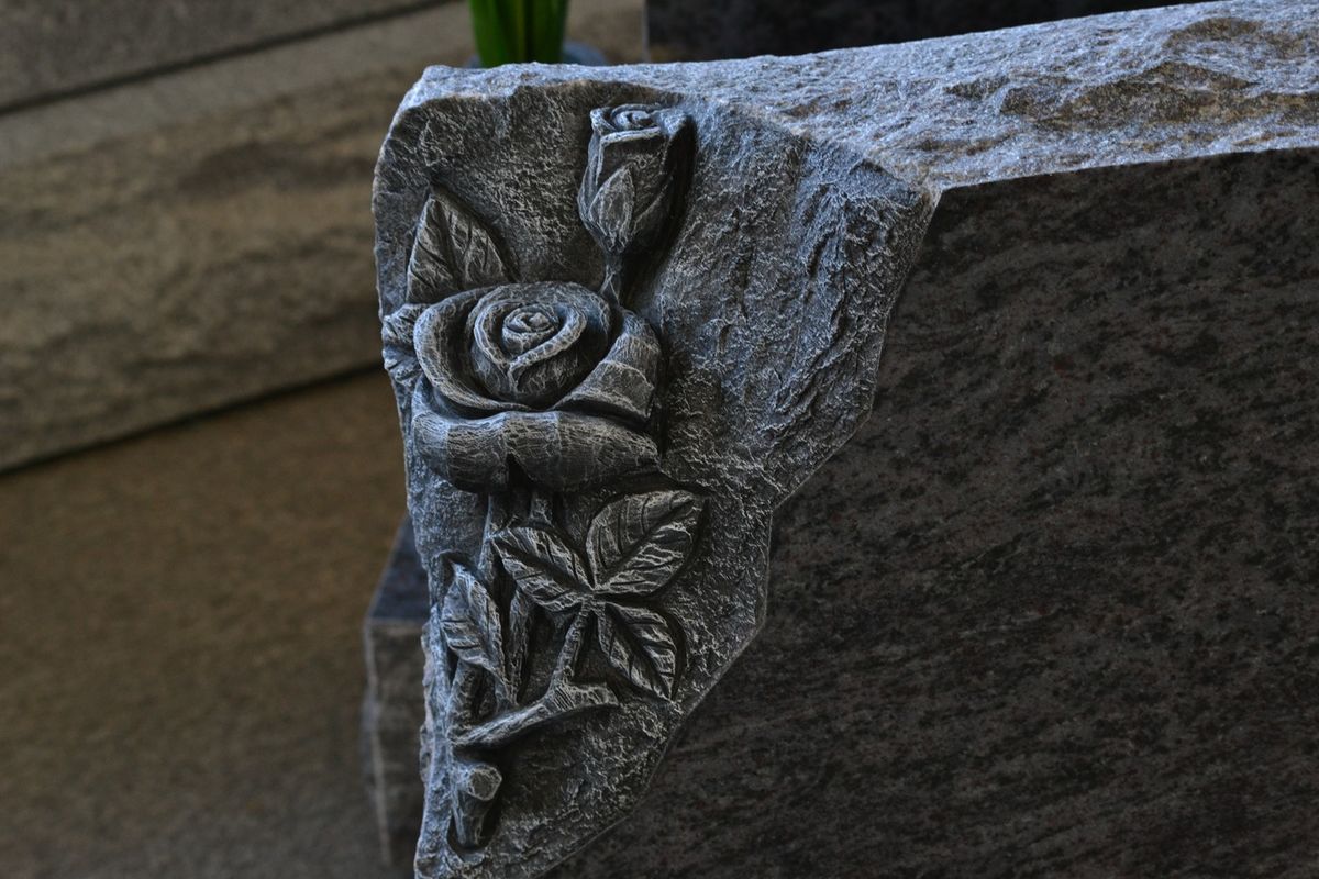 Polished black granite upright monument with floral arrangement at cemetery
